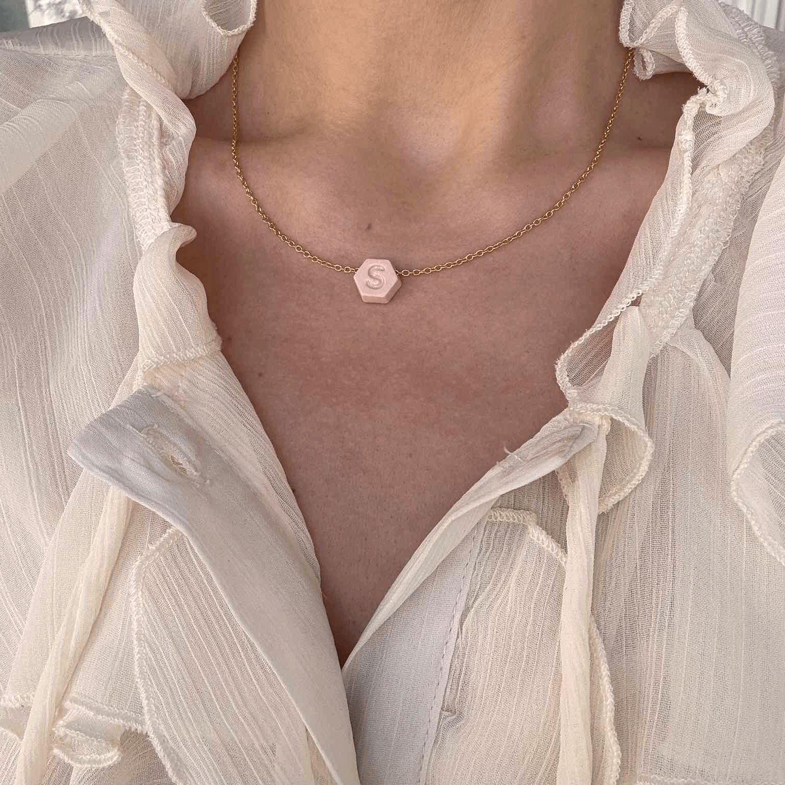 Woman wearing a dainty custom initial necklace with pink hexagon porcelain pendant and gold chain, styled with ivory blouse – summer jewelry gift for her.