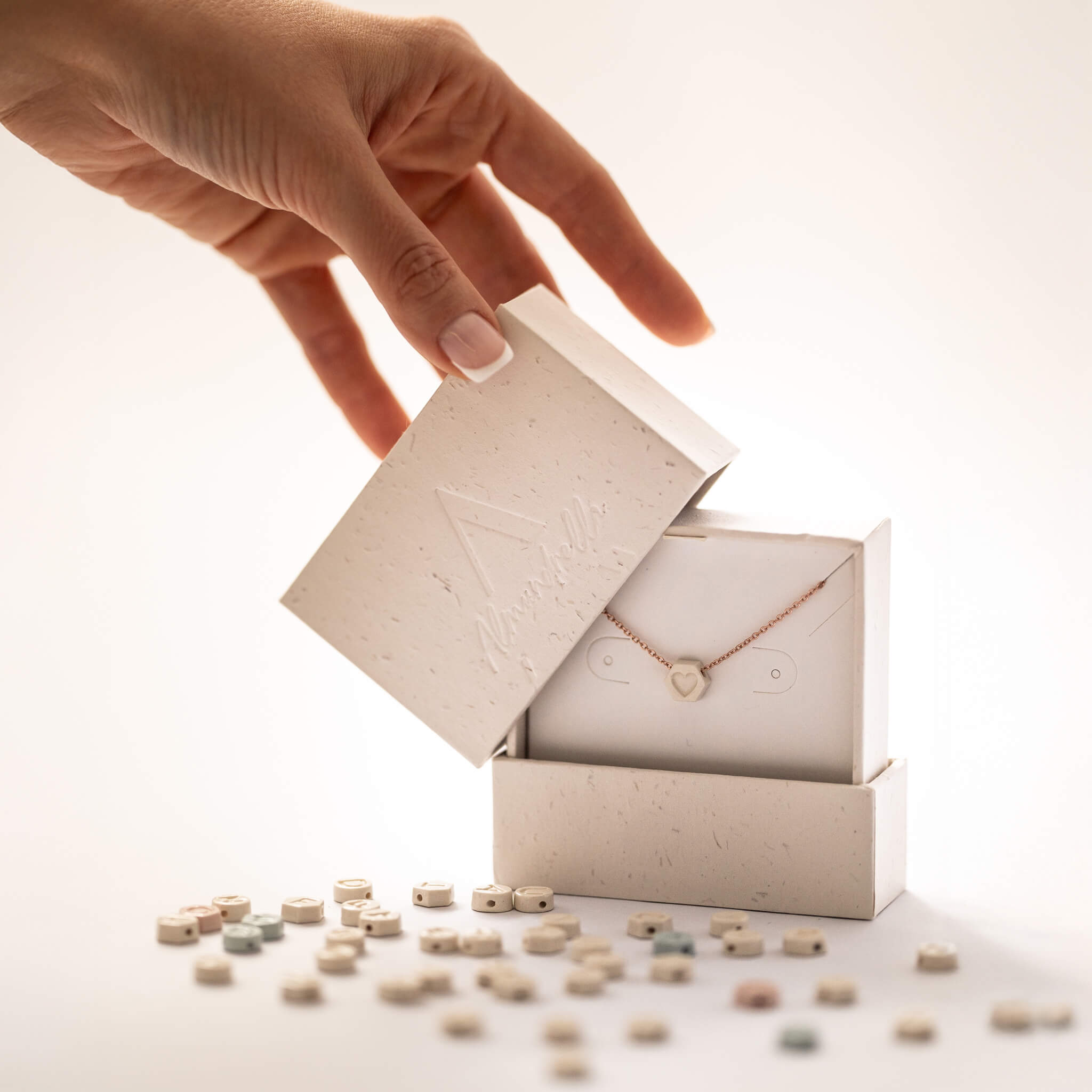 Opening eco box with personalized porcelain necklace and ceramic charms scattered – Almundrella