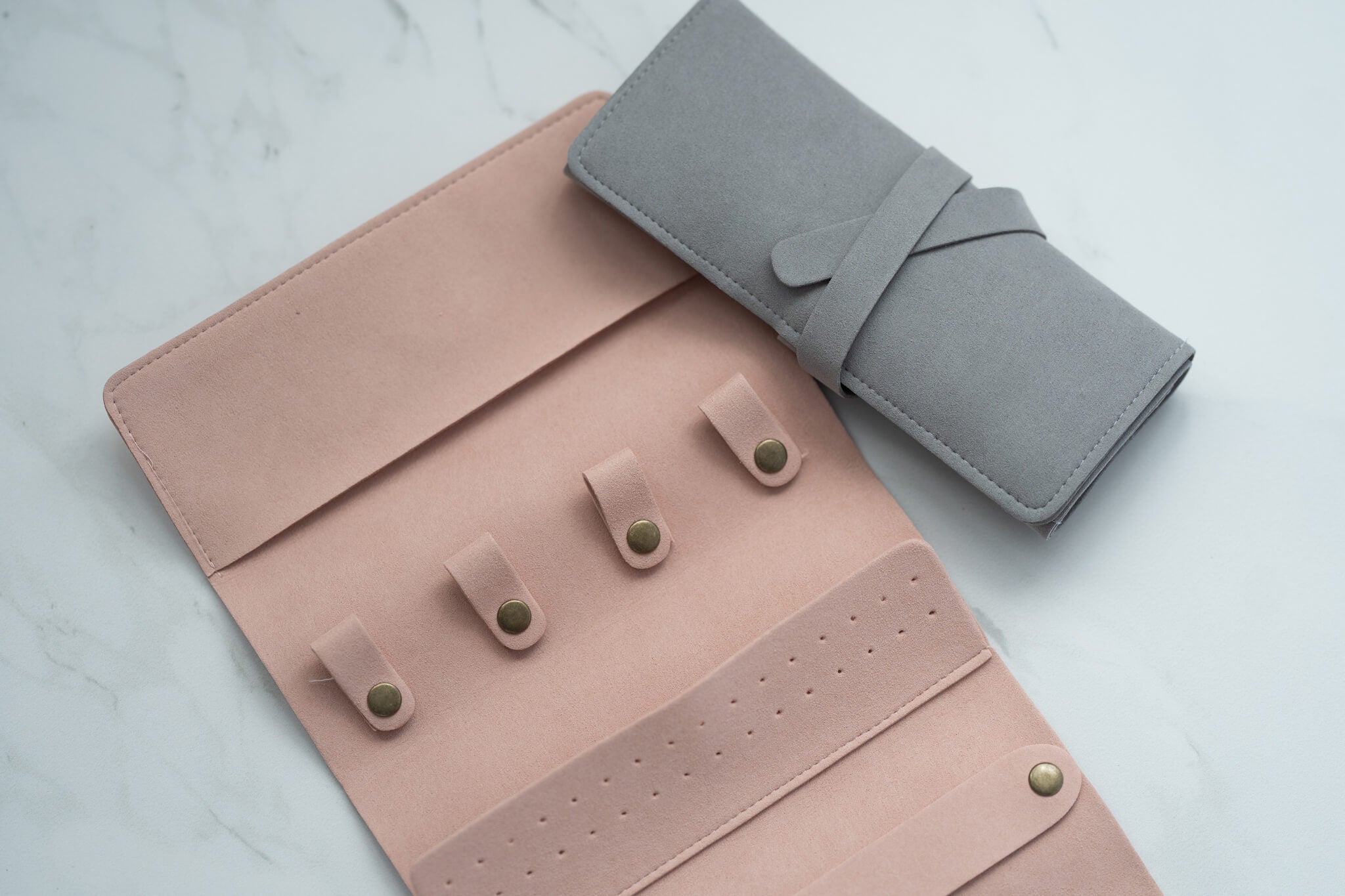 Detail of pink and gray jewelry organizers showing snap fasteners and soft suede texture.