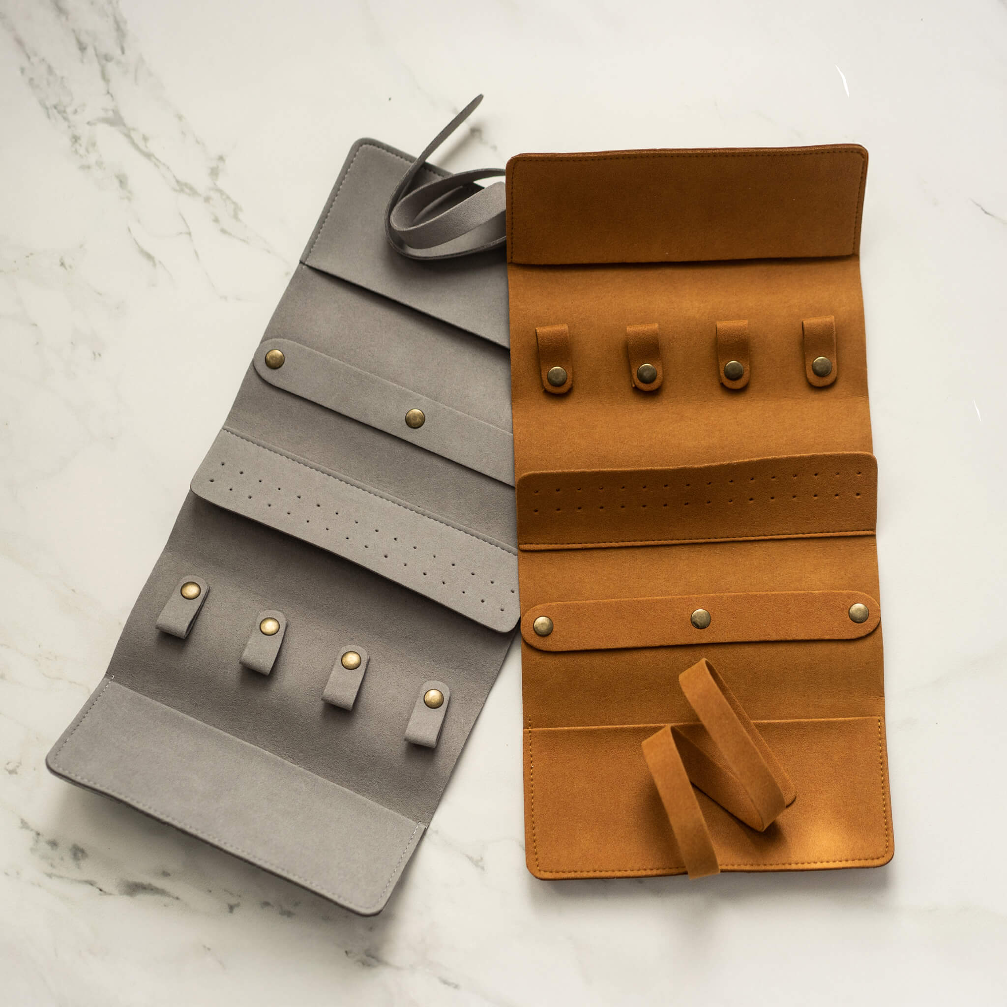 Open suede-like jewelry travel organizers in gray and camel, showing ring and necklace storage compartments