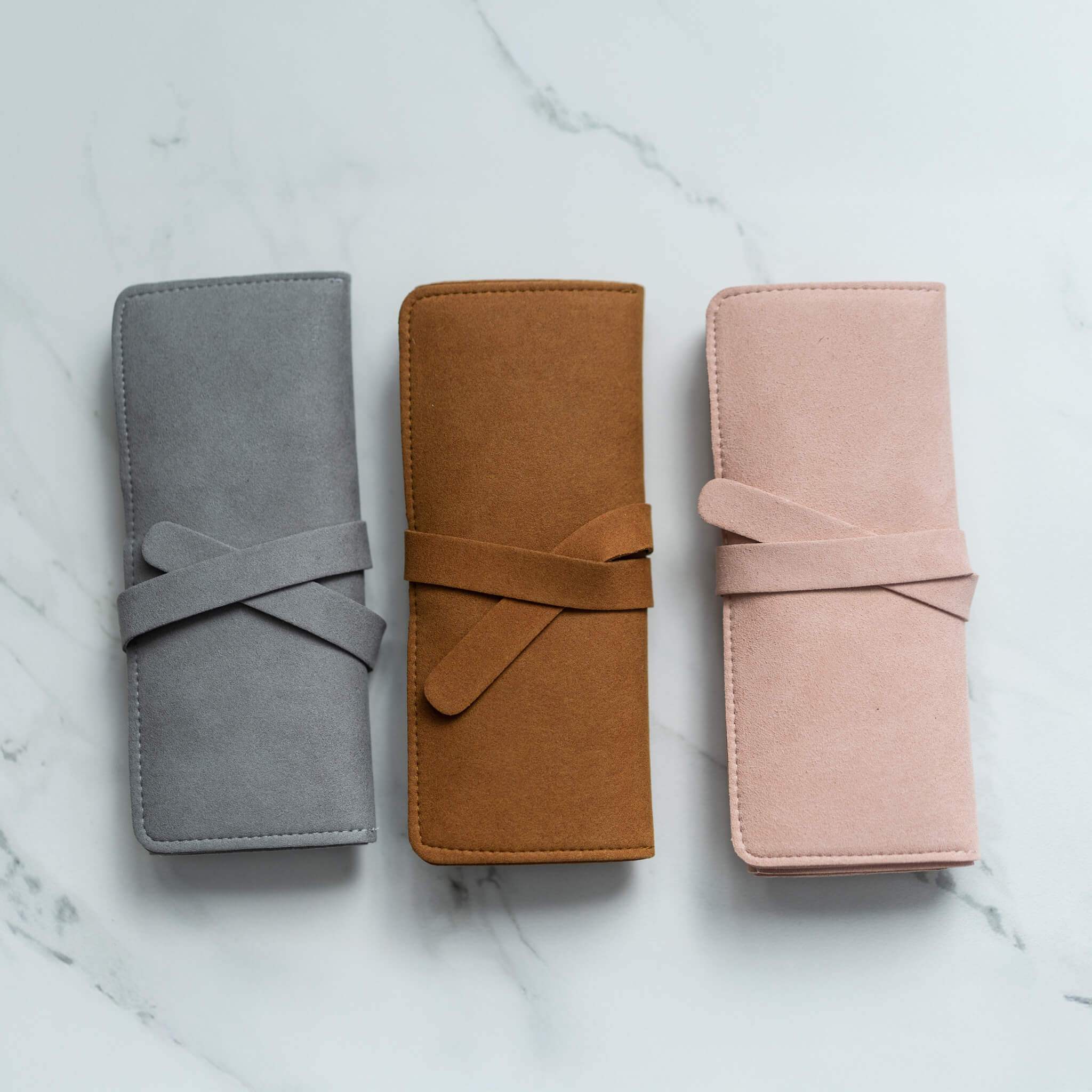 Rolled suede jewelry organizers in gray, camel, and blush pink with tie closures