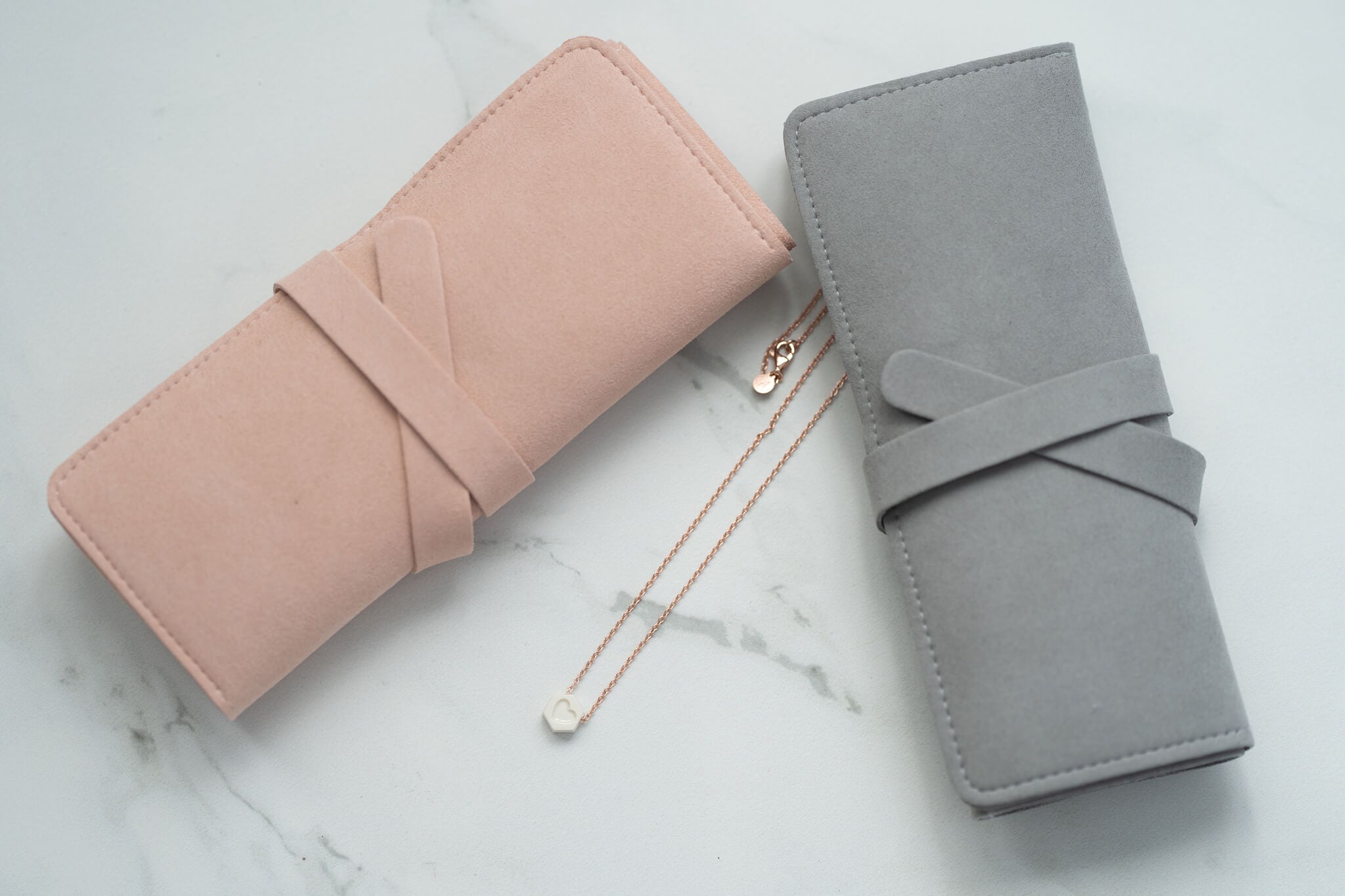 Almundrella heart necklace placed between rolled blush and gray travel jewelry bags