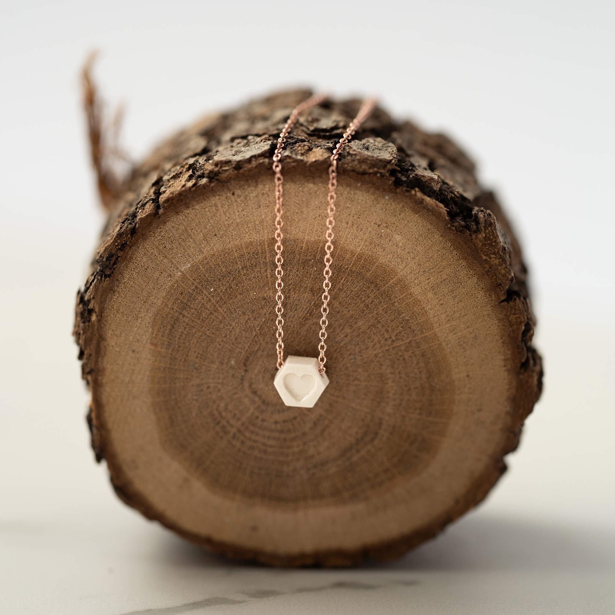 Handmade porcelain heart necklace displayed on natural wood piece.