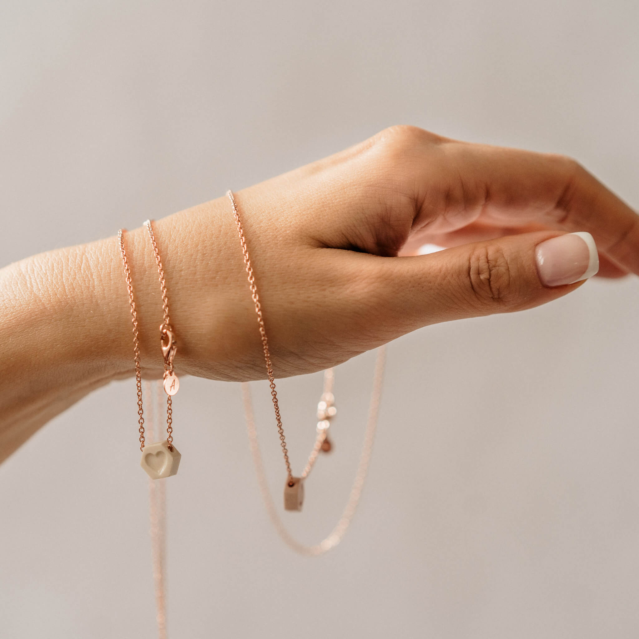 Delicate rose gold-plated porcelain heart necklace shown wrapped around a woman's hand.